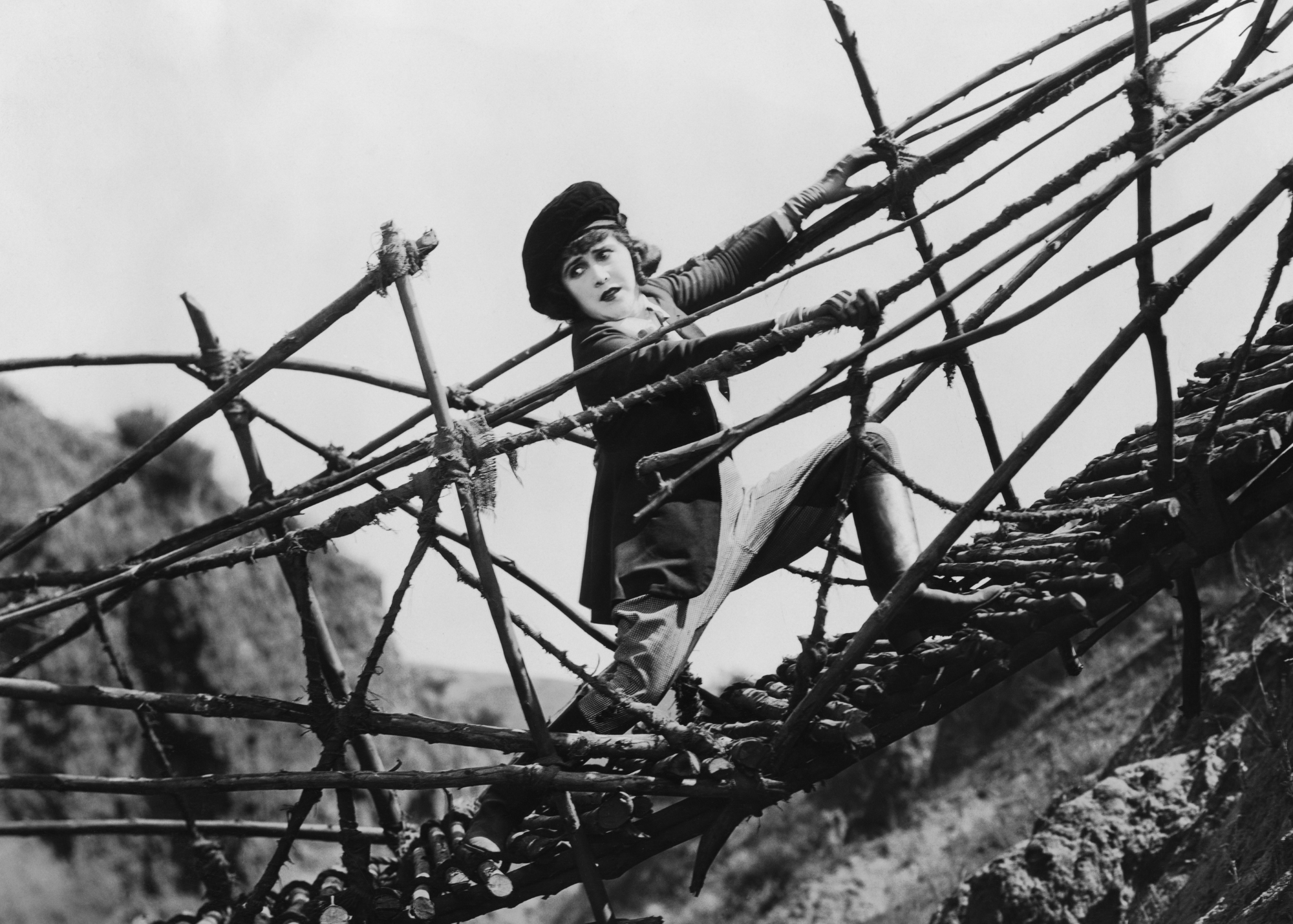Person in black and white film clinging to falling bridge